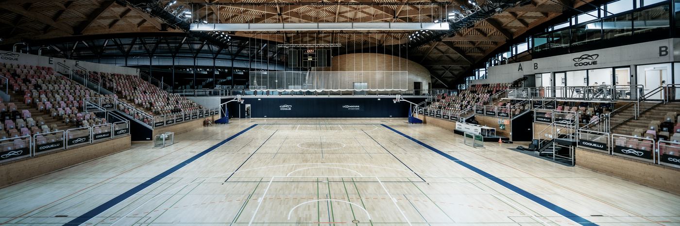 An indoor sports court with a wooden floor and tiered seating