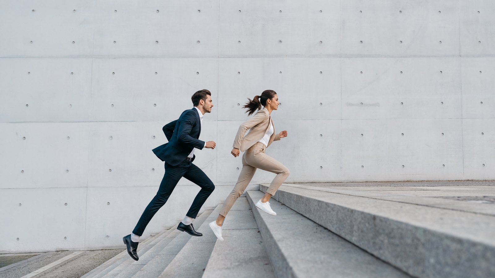 Two colleagues in business clothes running up concrete steps. Move together, perform better.